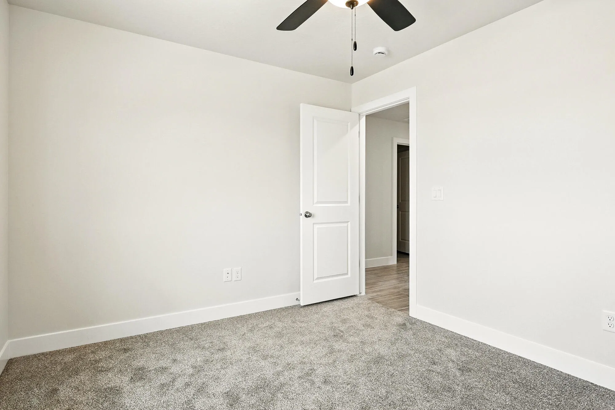 Empty room featuring light colored carpet, ceiling fan, and a smoke detector