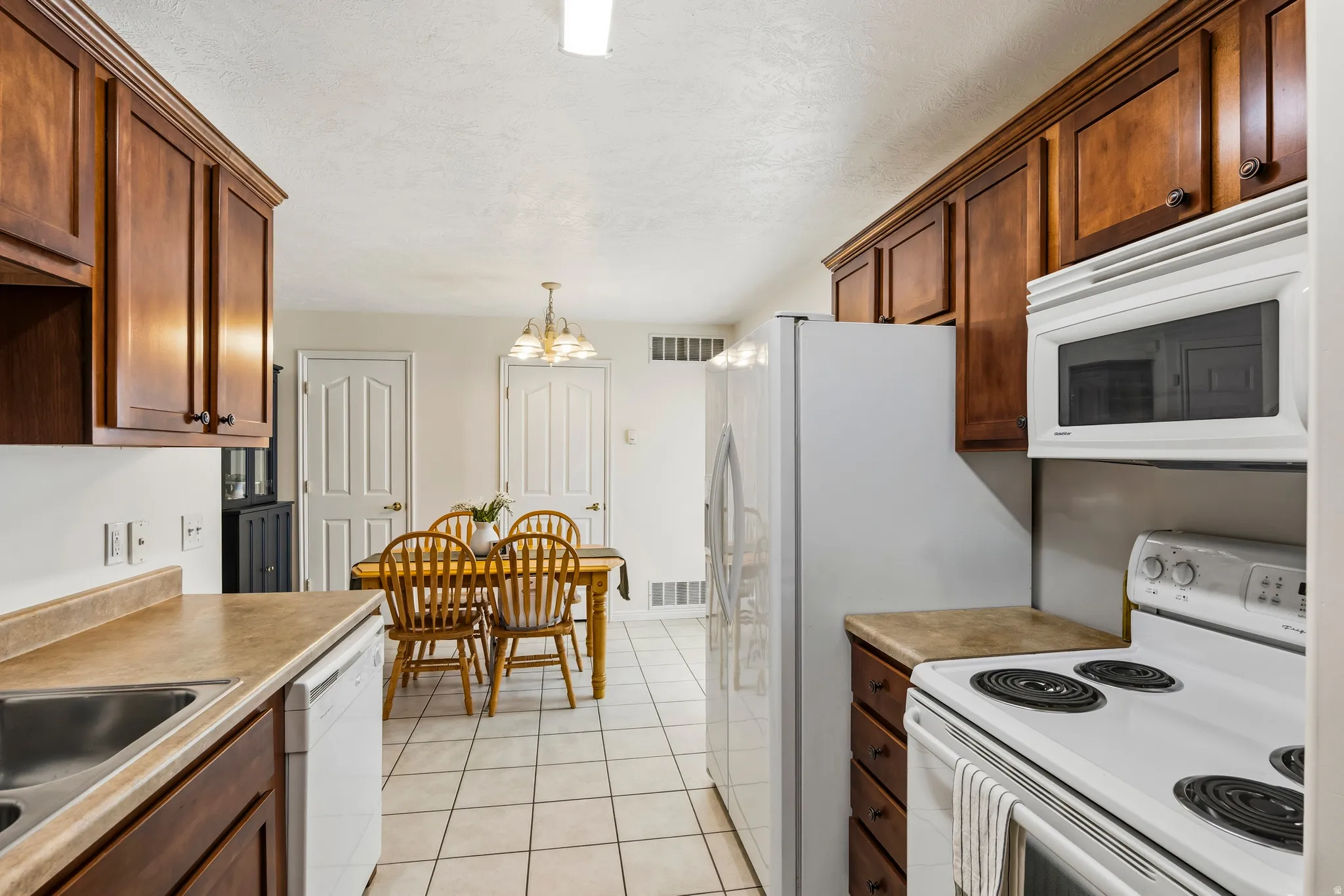 Kitchen with white appliances, light tile patterned flooring, light countertops, a textured ceiling, and hanging lights