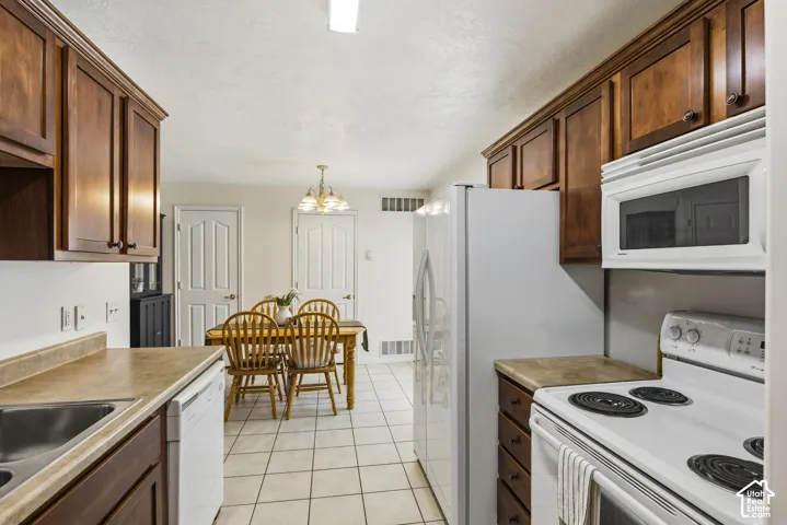 Kitchen with white appliances, light tile patterned flooring, light countertops, a textured ceiling, and hanging lights
