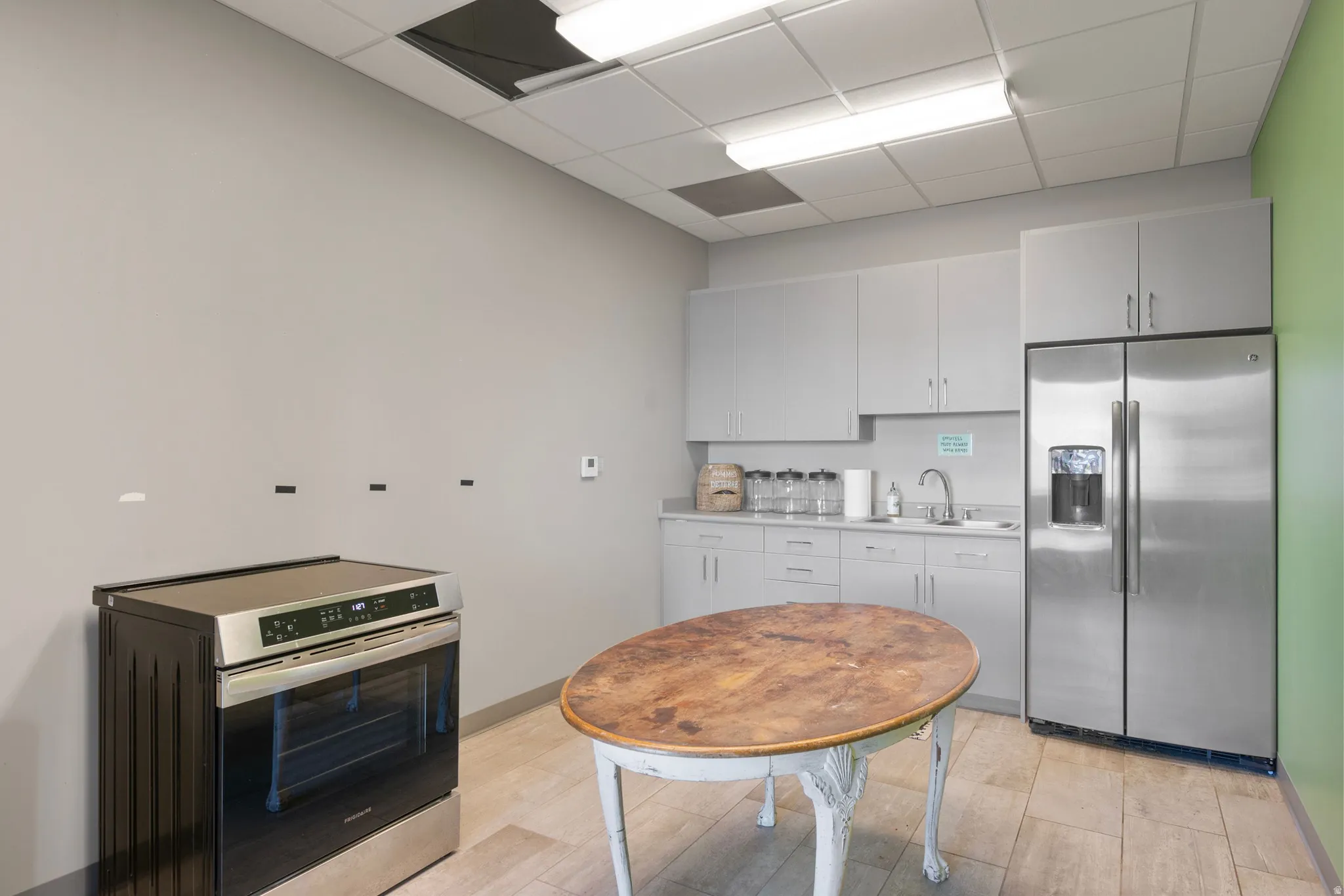 Kitchen with stainless steel appliances, light countertops, a drop ceiling, light wood finished floors, and white cabinets