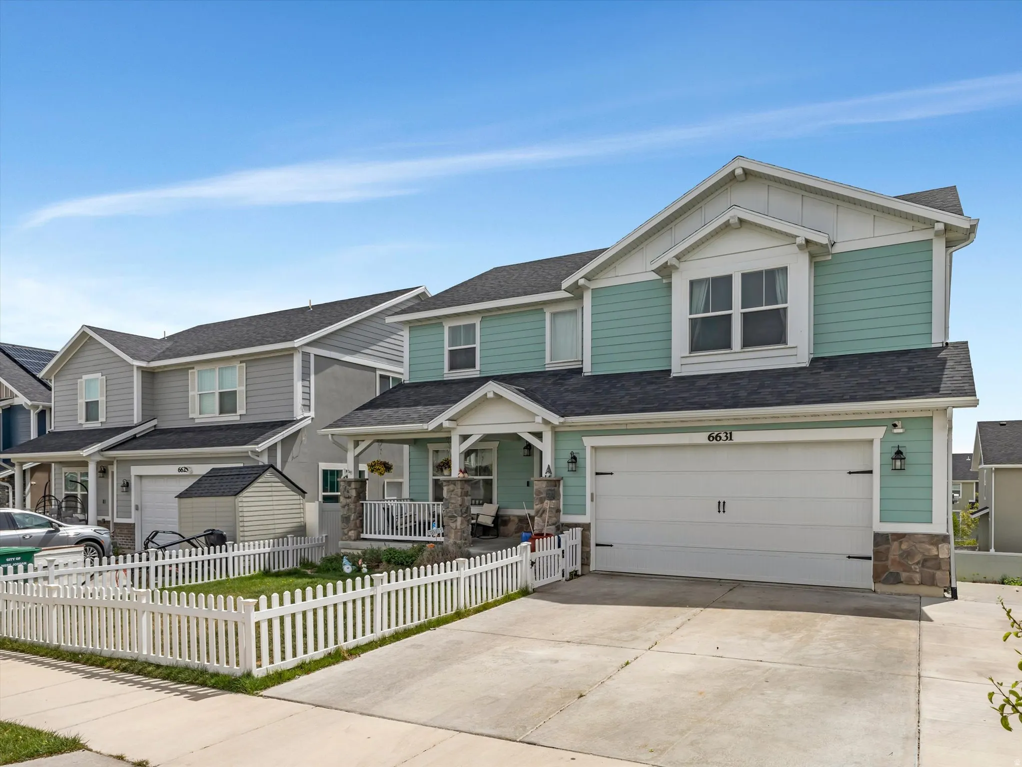Craftsman-style home featuring covered porch, an attached garage, driveway, stone siding, and a fenced front yard