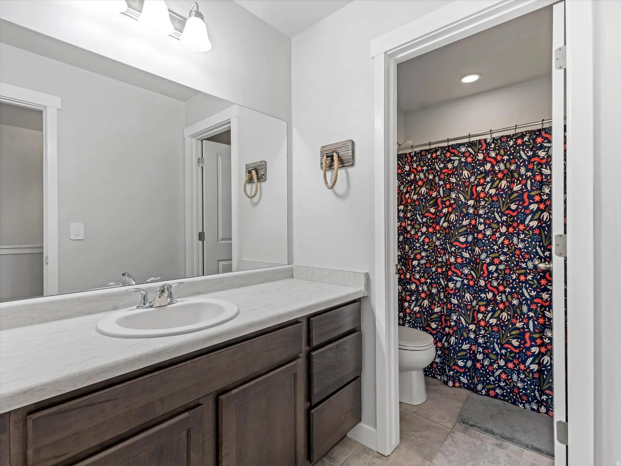 Full bathroom with a shower with shower curtain, vanity, light tile patterned floors, and recessed lighting