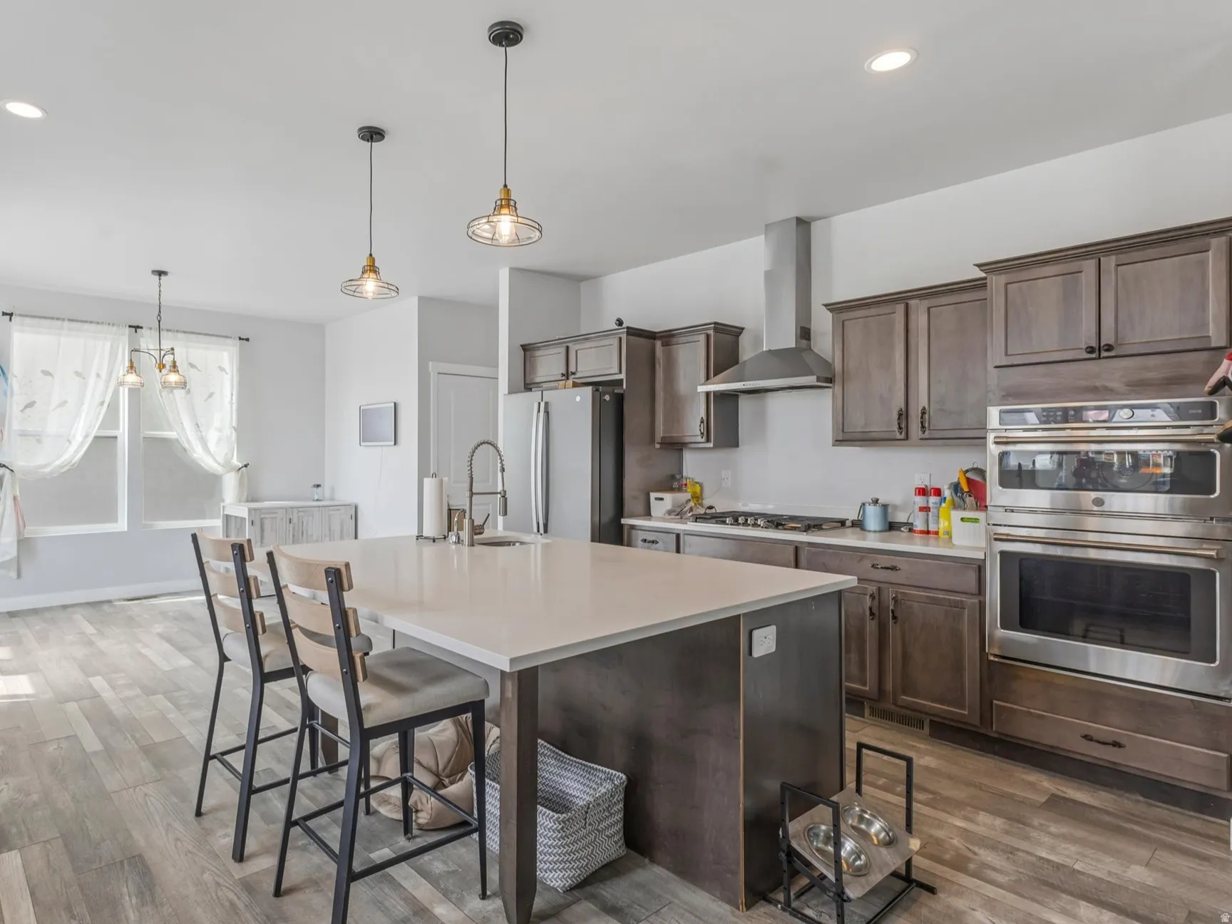 Kitchen with stainless steel appliances, dark wood finish cabinetry, light wood finished floors, a kitchen island with sink, and a breakfast bar area