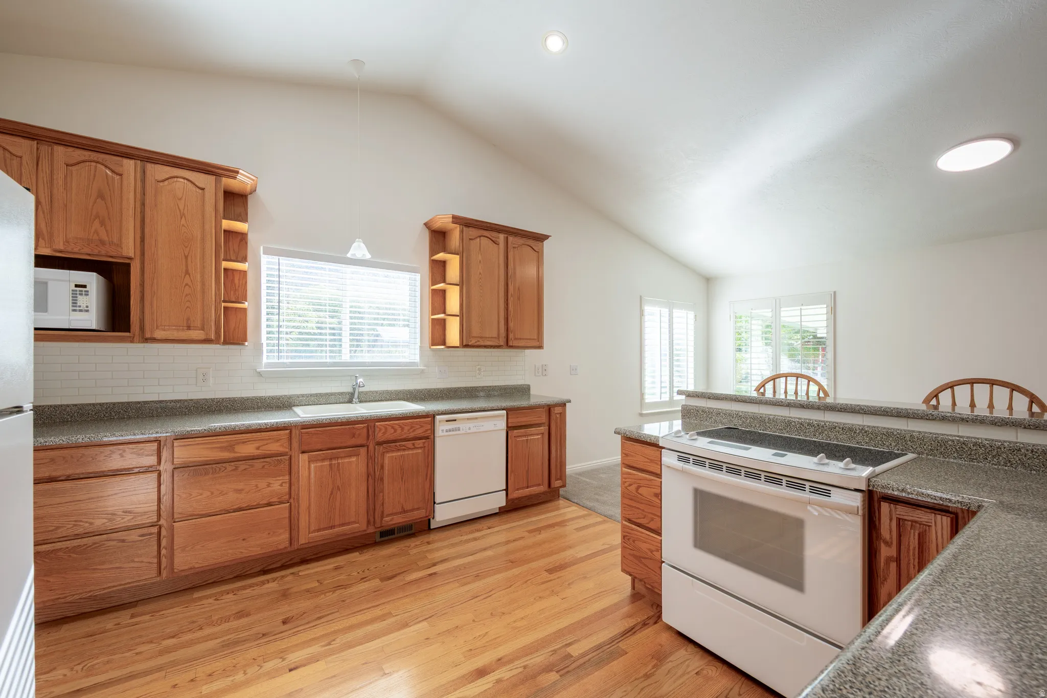 Kitchen featuring white appliances, dark countertops, light wood finished floors, wood finish cabinetry, and lofted ceiling
