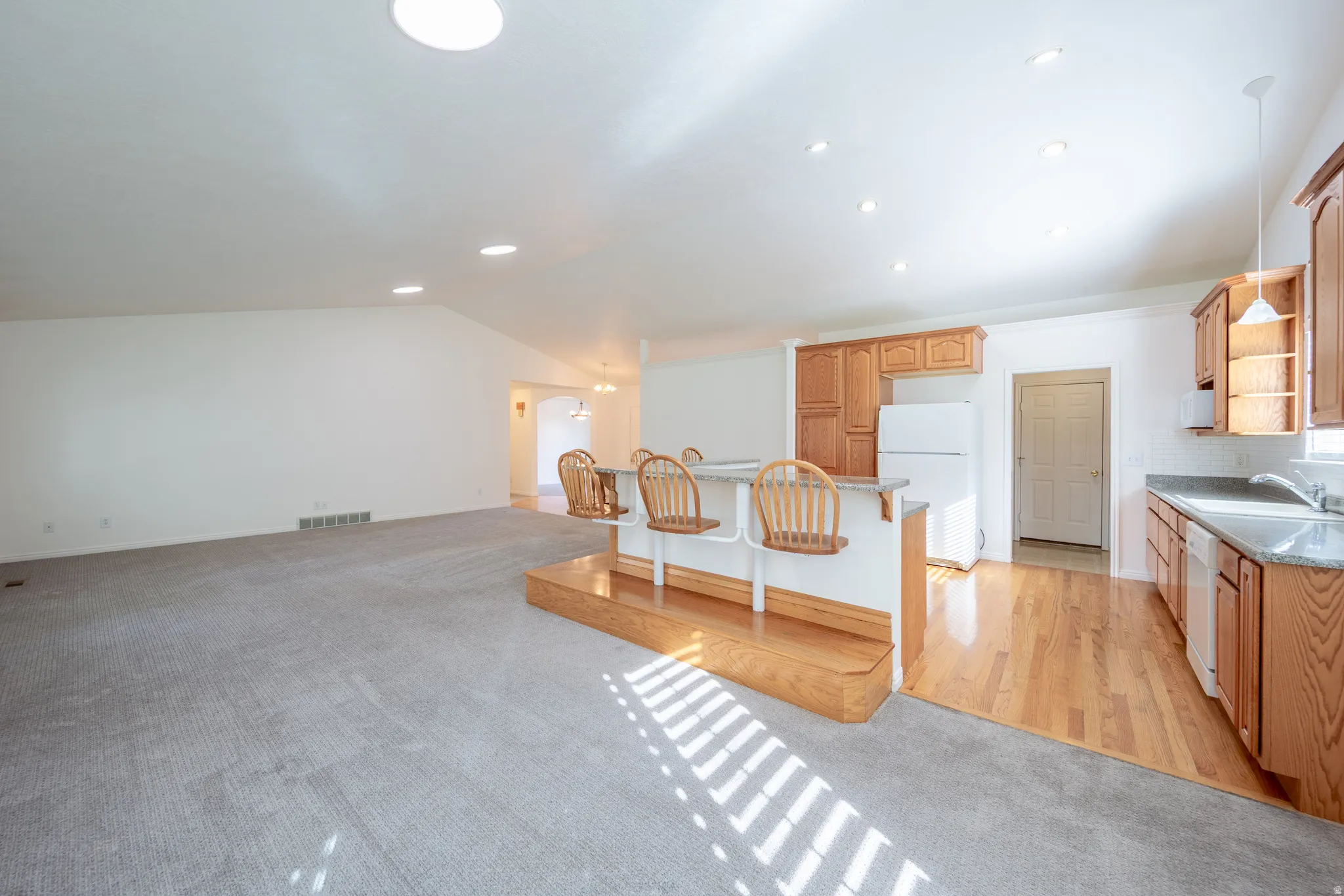 Kitchen featuring light carpet, white appliances, a breakfast bar area, vaulted ceiling, and open floor plan
