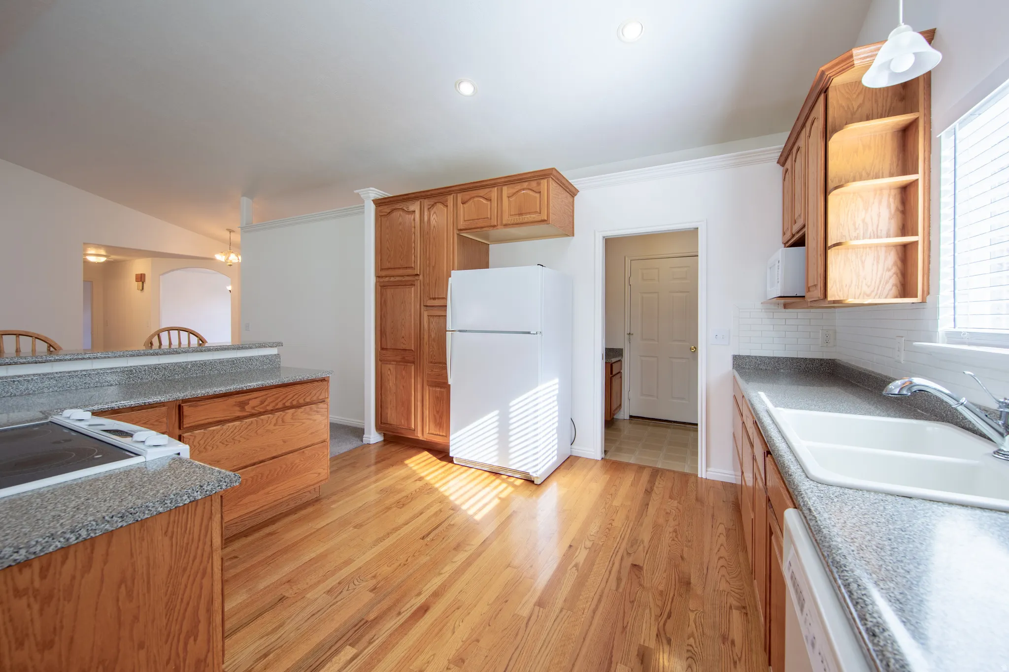Kitchen with white appliances, open shelves, wood finish cabinetry, backsplash, and light wood-style flooring