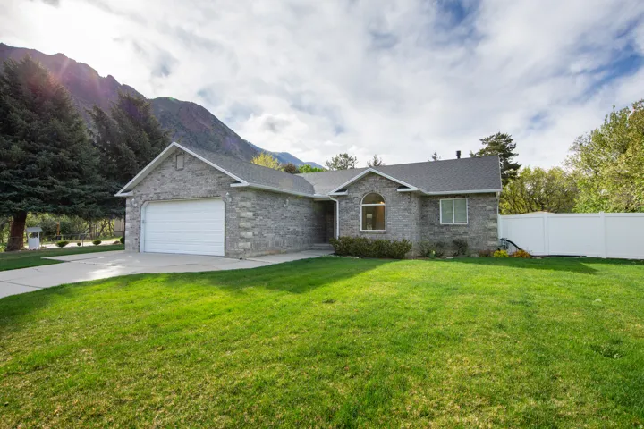 Ranch-style house with an attached garage, driveway, brick siding, a shingled roof, and a mountain view