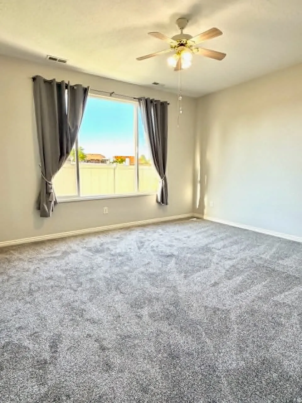 Spacious room featuring neutral-toned walls, plush gray carpeting, and a large window