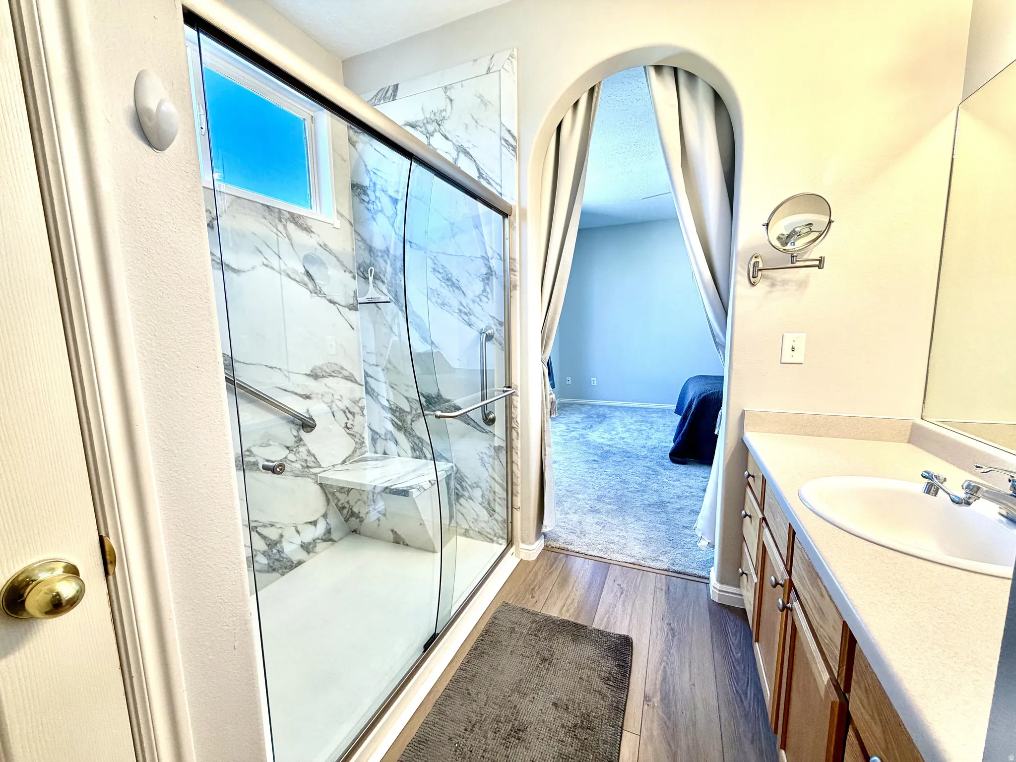 Glass-enclosed shower with a built-in bench, marble-finish tile, and a window for natural light