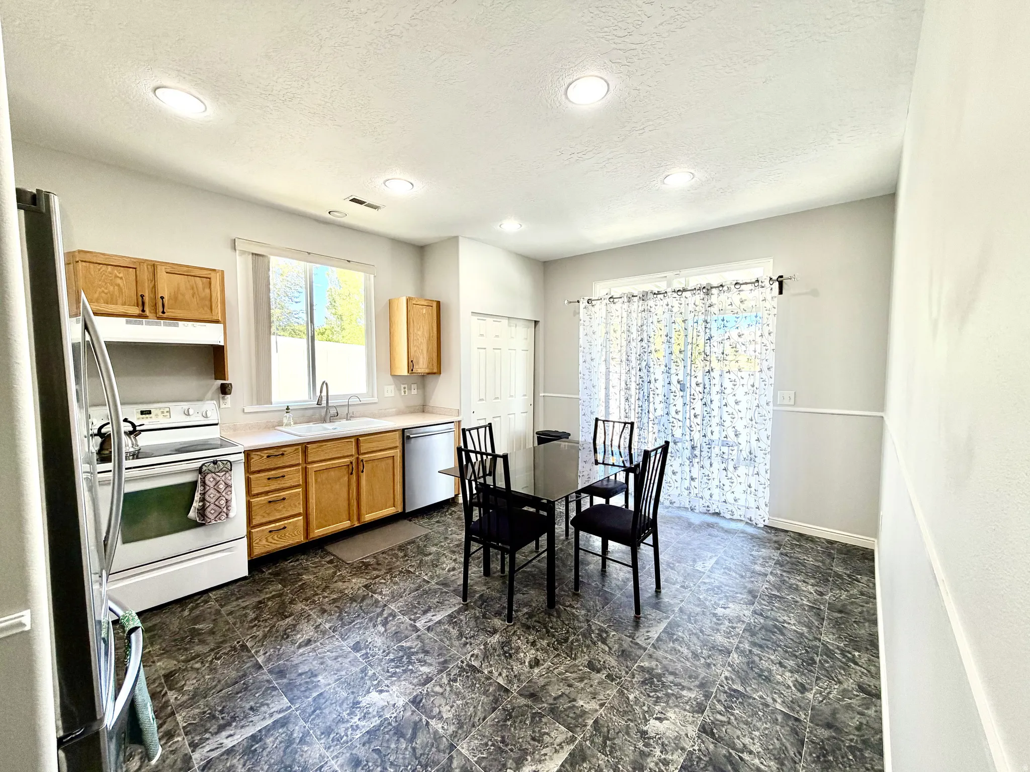 Kitchen featuring recessed lighting, natural wood cabinetry, a stainless steel refrigerator, white range, and a sliding glass door