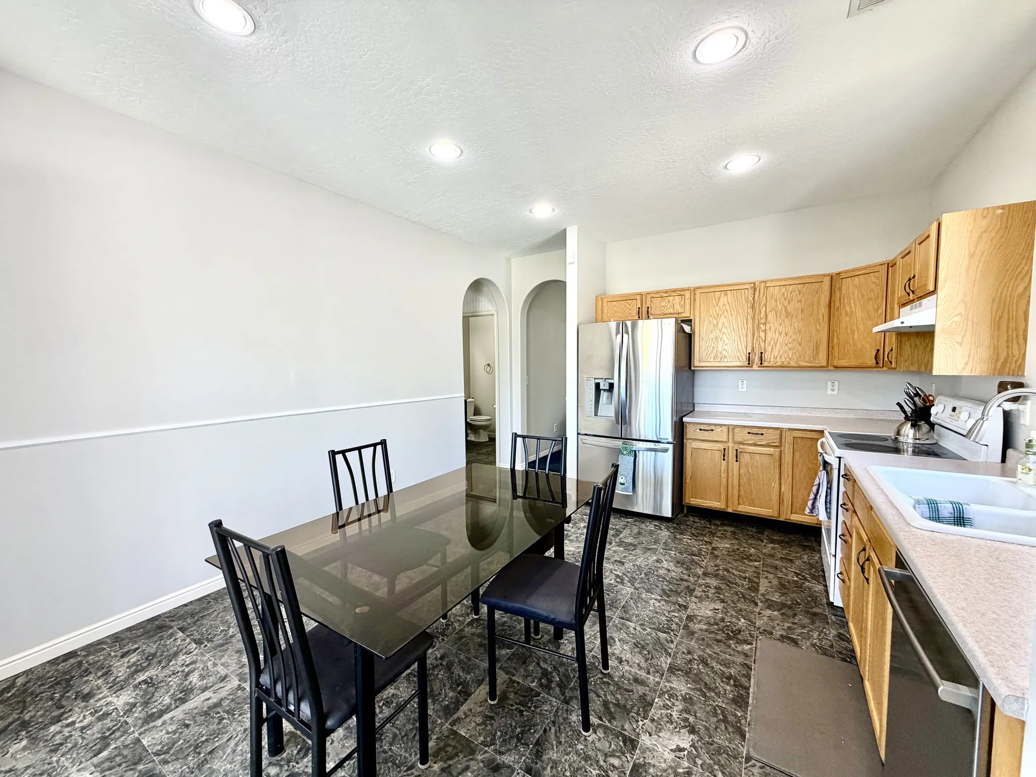 Kitchen and dining area featuring wood cabinetry, stainless steel refrigerator, white wall paneling, and dark patterned flooring