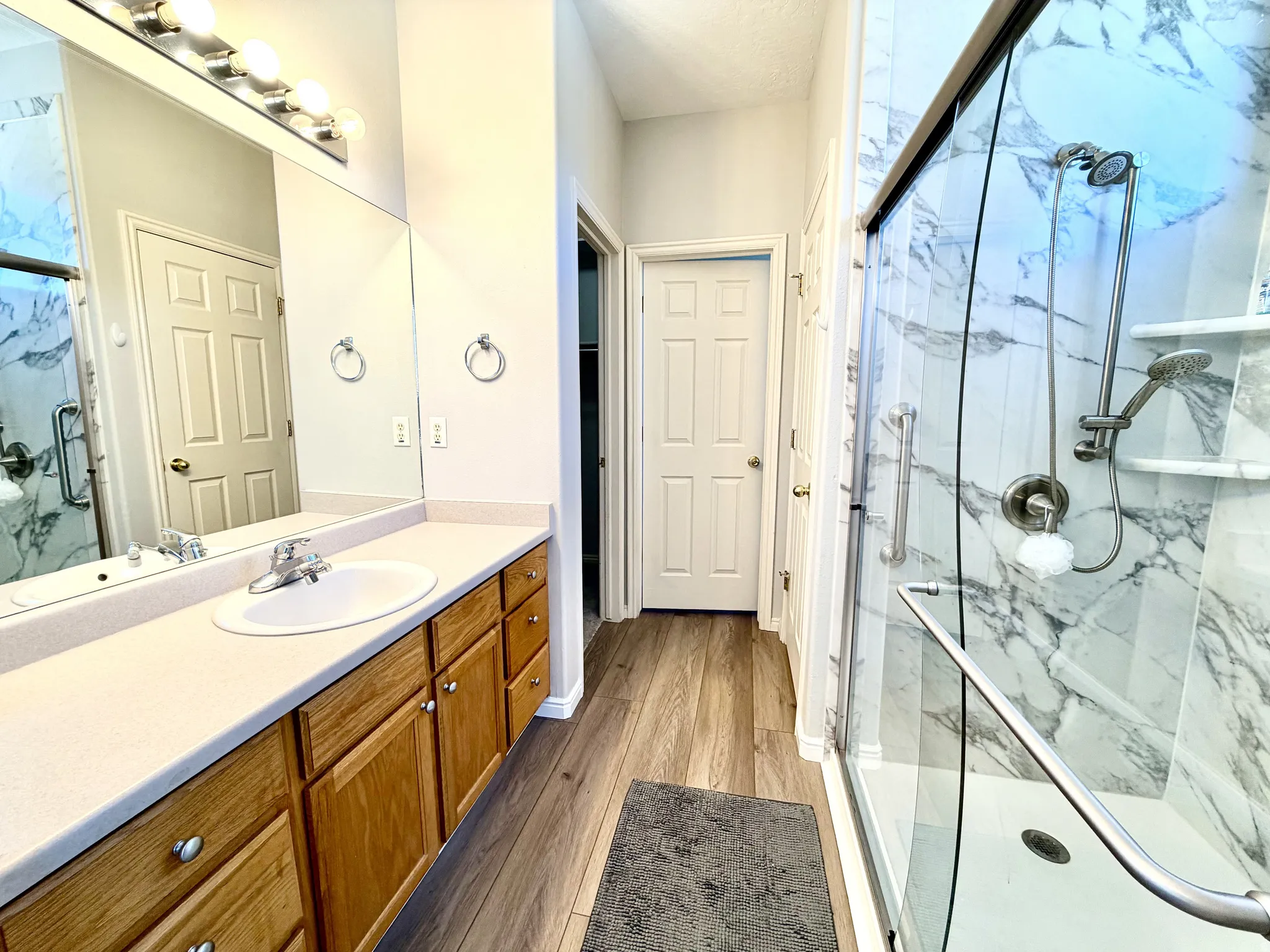 Spacious bathroom featuring a double vanity with wood cabinetry, a large mirror, and a glass-enclosed shower with a marble-look tile surround and dual shower heads
