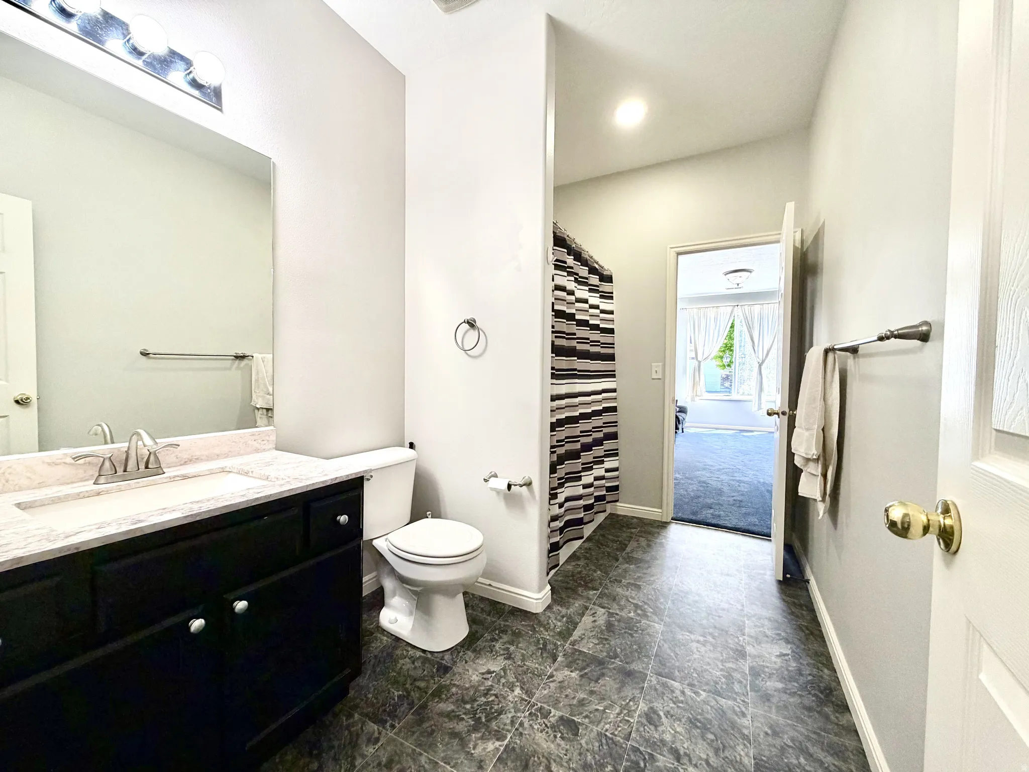 Bathroom featuring a dark vanity with a light countertop, a white toilet, and dark patterned flooring