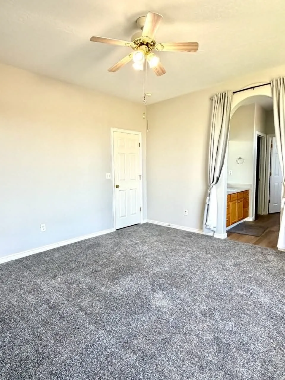 Spacious room with plush gray carpeting, a ceiling fan with integrated lighting, and neutral wall tones