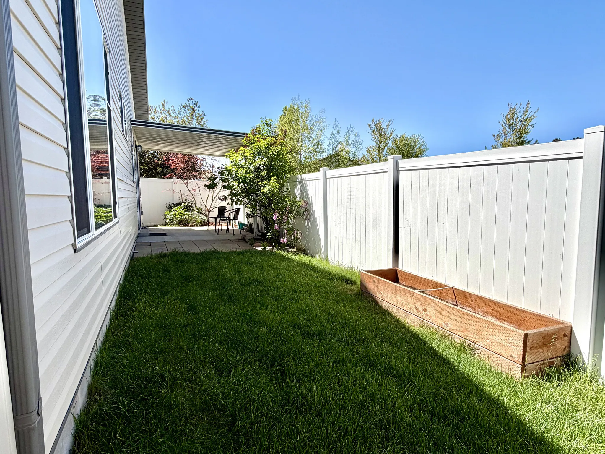 Landscaped side yard featuring a covered patio, white privacy fencing, a raised planter box, and a manicured lawn
