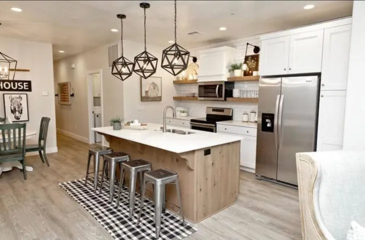 Kitchen with open shelves, stainless steel appliances, a breakfast bar area, light wood-style flooring, and a kitchen island with sink