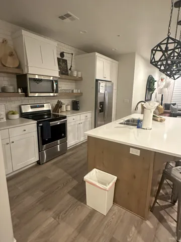 Kitchen featuring open shelves, decorative light fixtures, stainless steel appliances, tasteful backsplash, and dark wood-style flooring