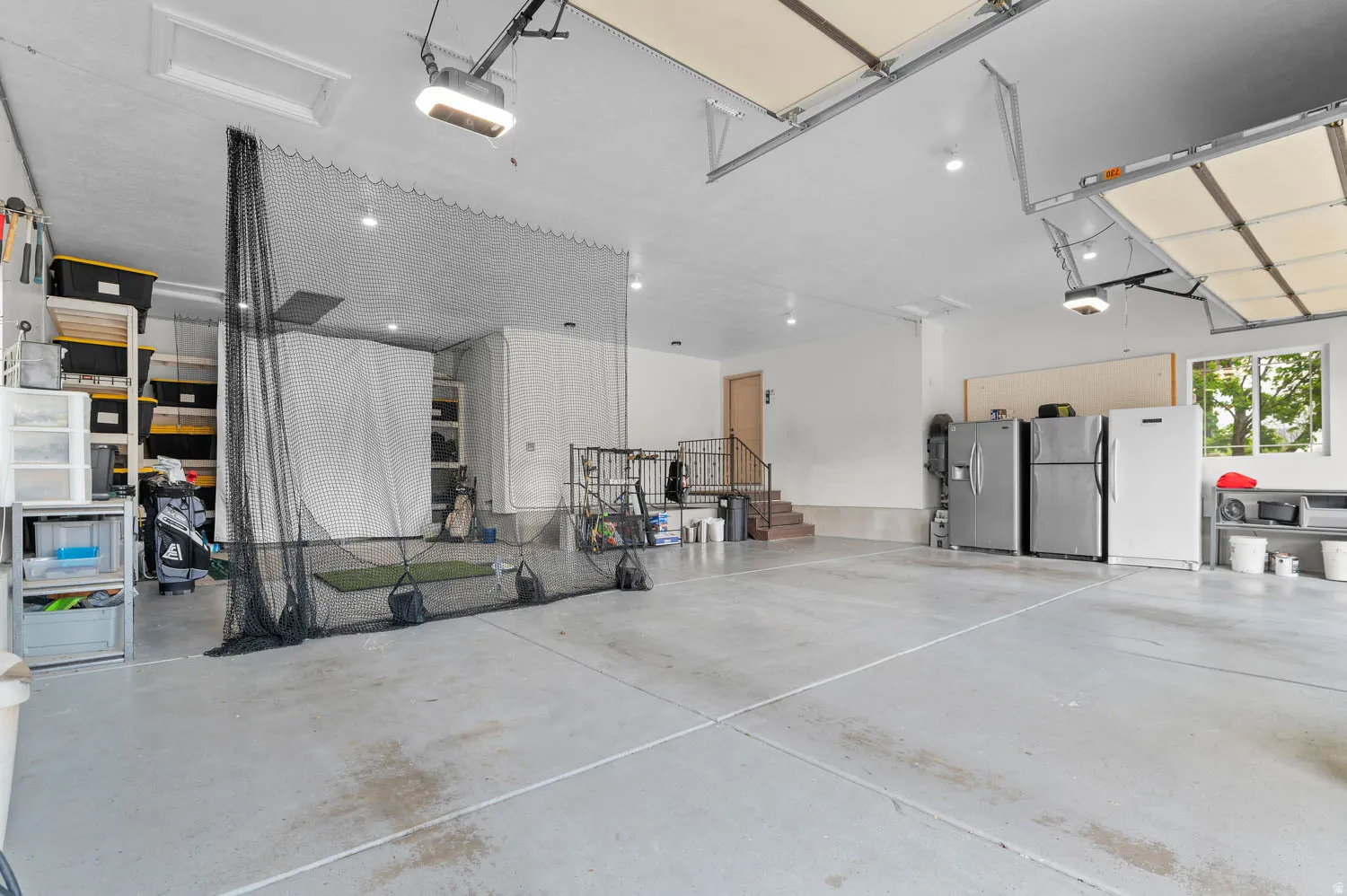 Garage featuring freestanding refrigerator, stainless steel refrigerator with ice dispenser, and a garage door opener