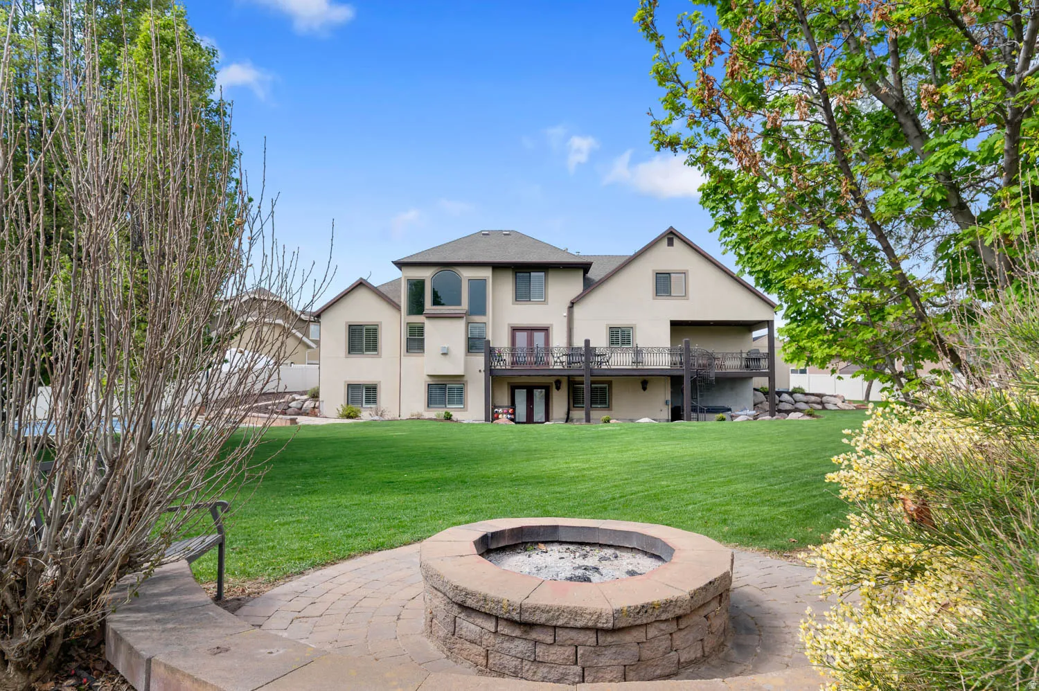 Rear view of property featuring a yard, stucco siding, a fire pit, and a balcony