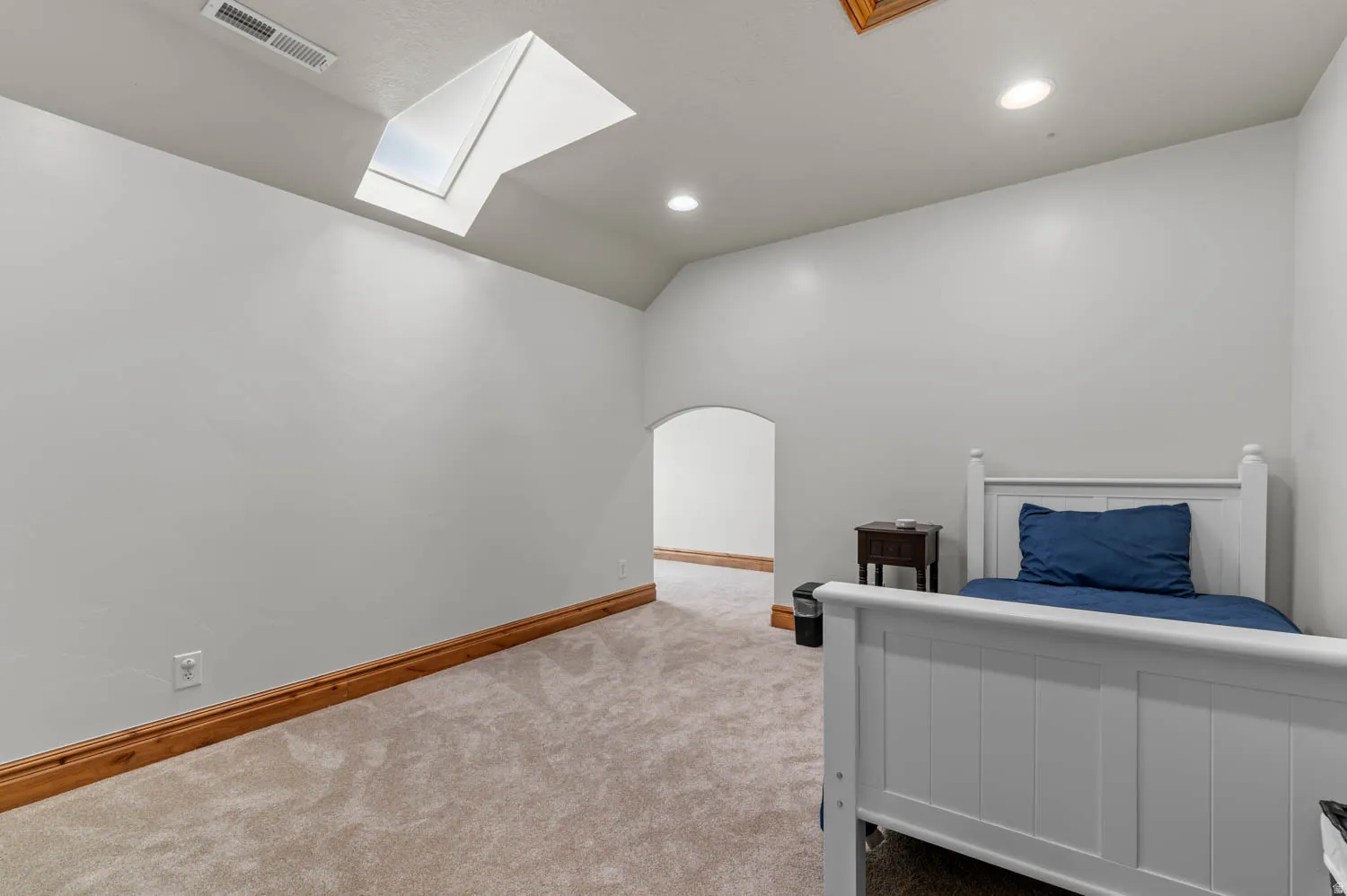 Carpeted bedroom with vaulted ceiling, recessed lighting, a skylight, and arched walkways