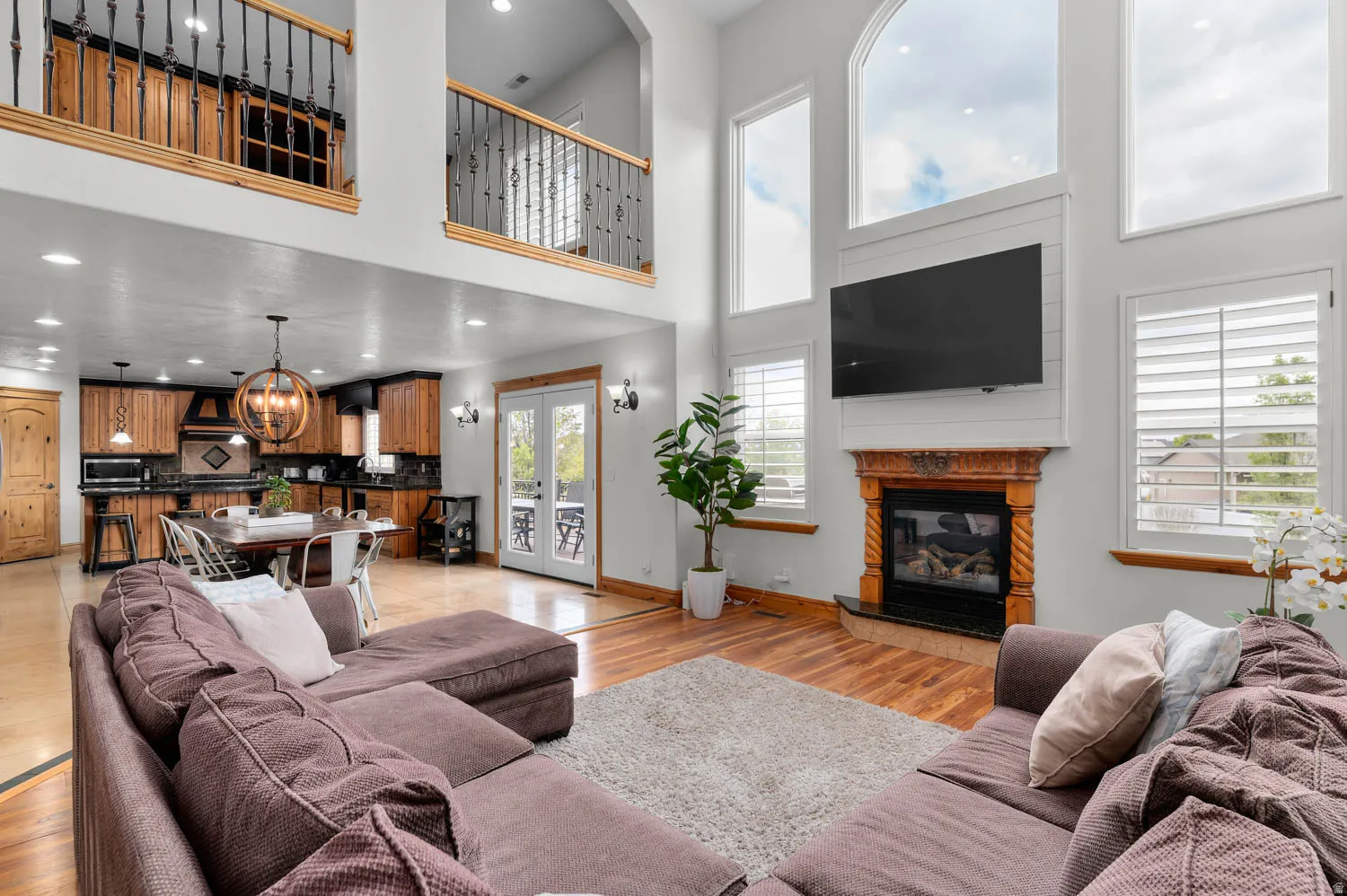 Living room with light wood-style flooring, a glass covered fireplace, suspended lighting, and a high ceiling