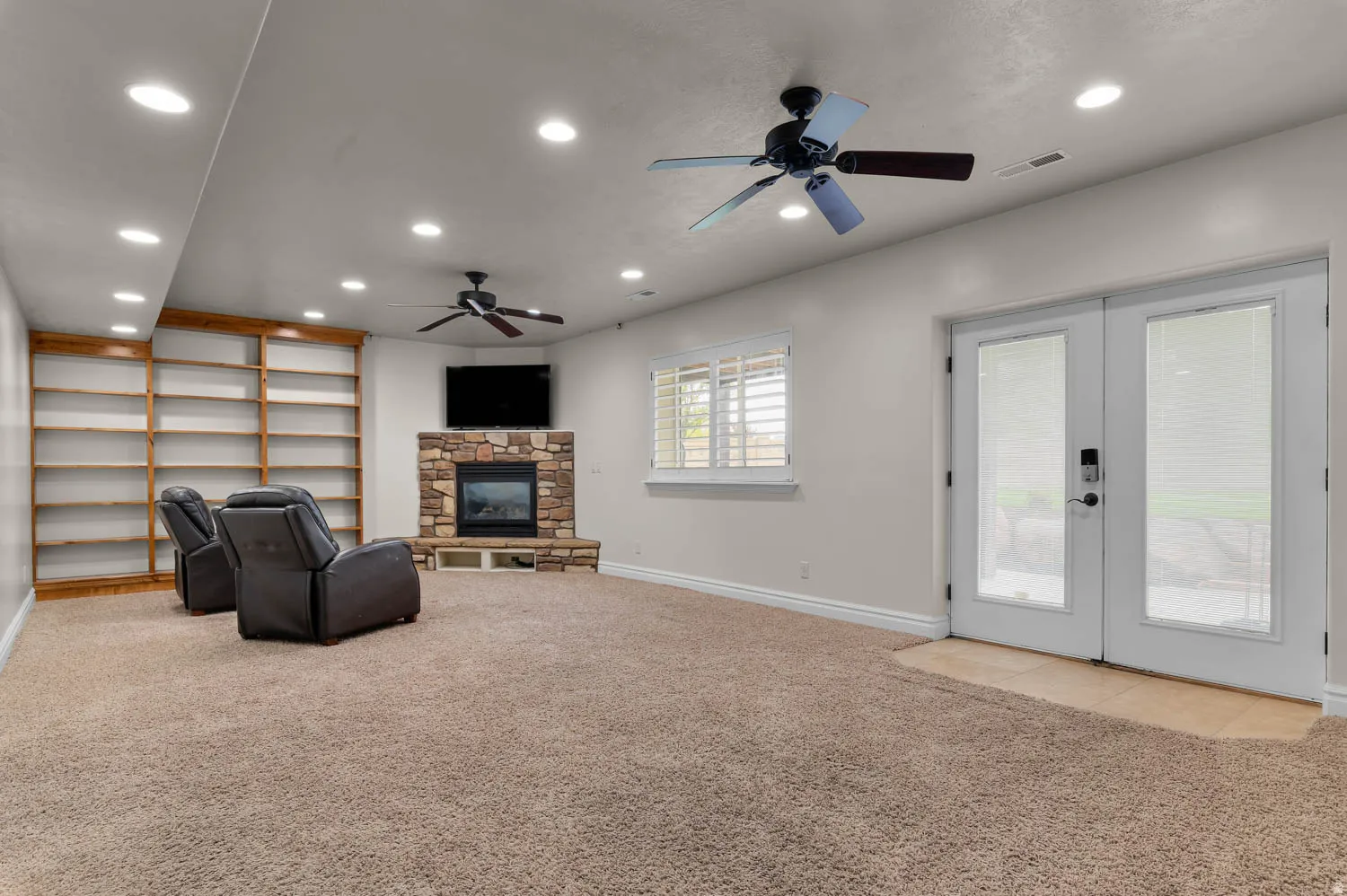 Unfurnished living room with light carpet, french doors, recessed lighting, a stone fireplace, and ceiling fan