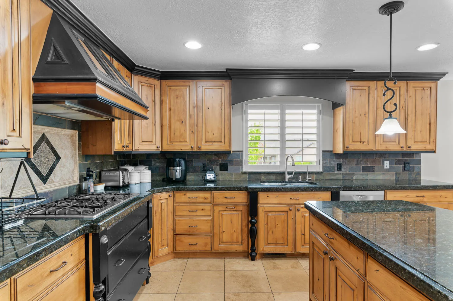 Kitchen featuring pendant lighting, light tile patterned floors, a textured ceiling, backsplash, and wood finish cabinetry