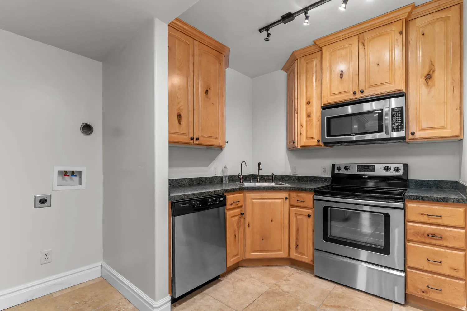 Kitchen featuring stainless steel appliances, rail lighting, light wood finish cabinets, and light tile patterned floors