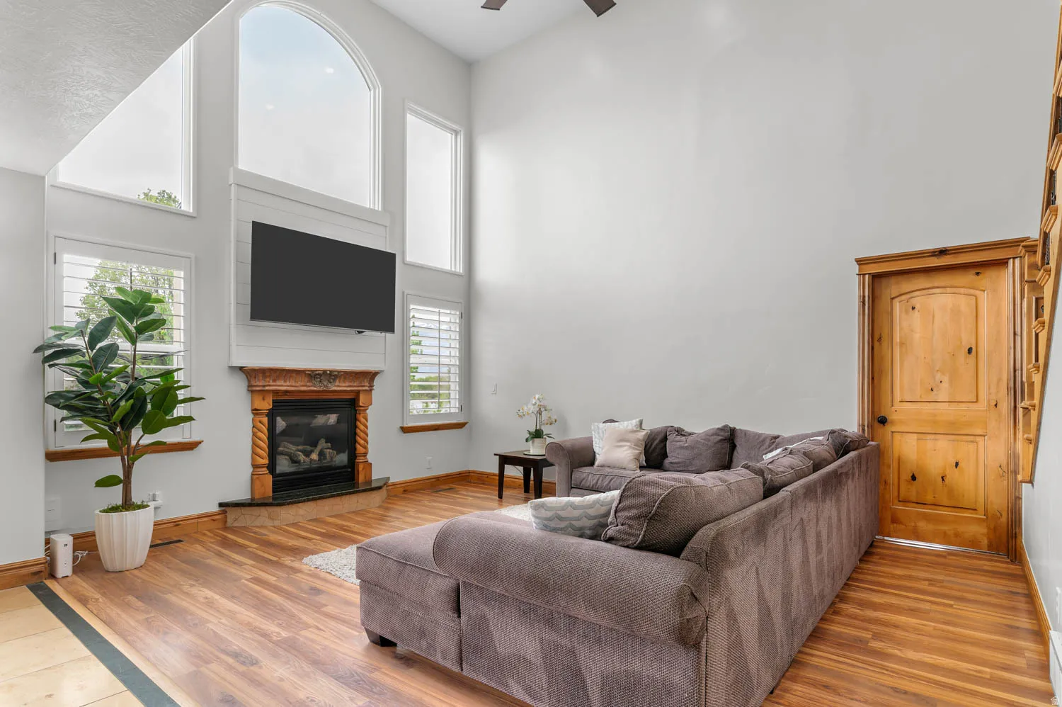 Living room with a glass covered fireplace, a high ceiling, light wood finished floors, and ceiling fan