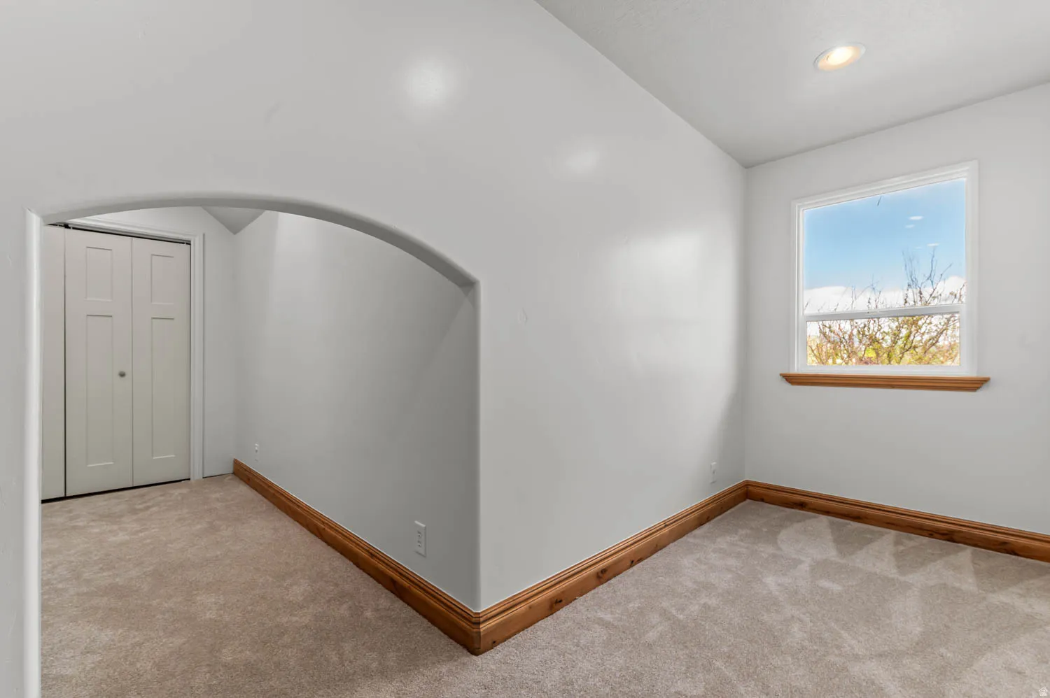 Empty room with light colored carpet, vaulted ceiling, recessed lighting, and arched walkways