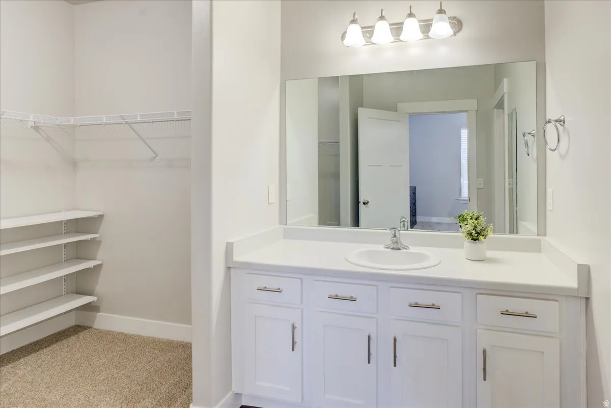 Full bath featuring vanity, light colored carpet, and a walk in closet