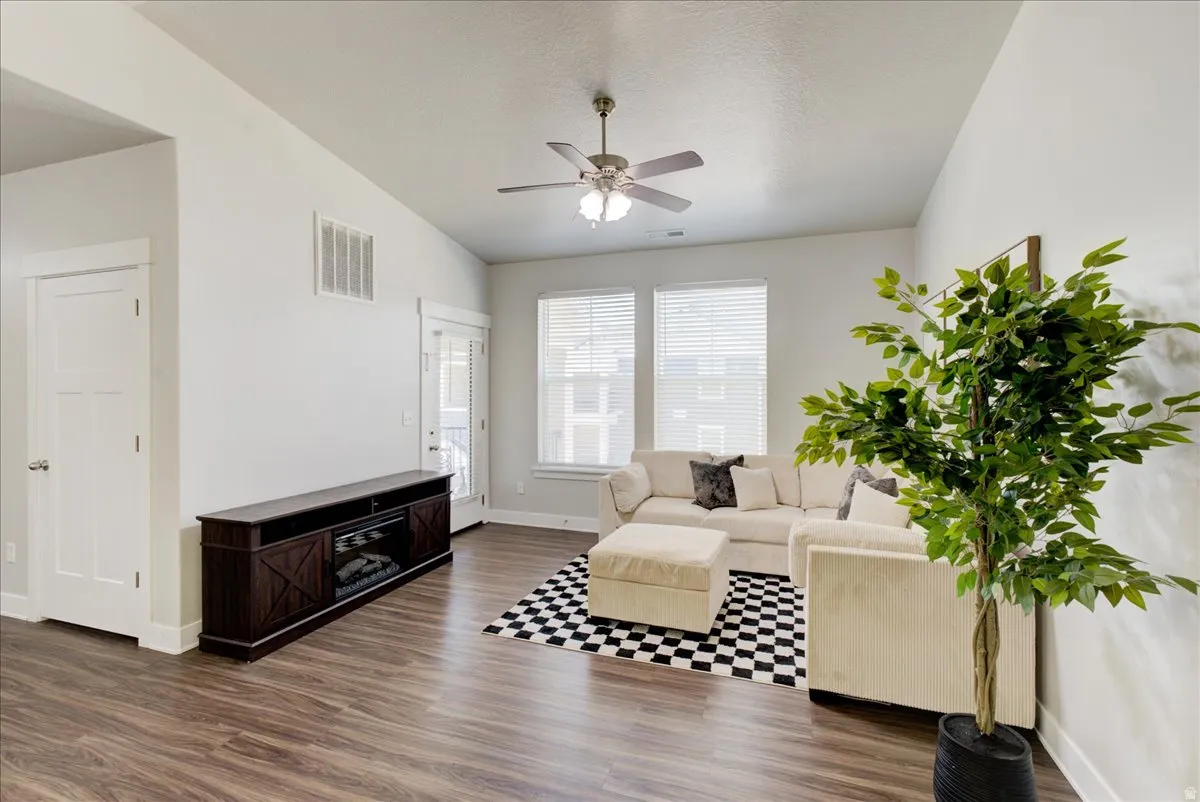 Living room with dark wood finished floors, a ceiling fan, and vaulted ceiling