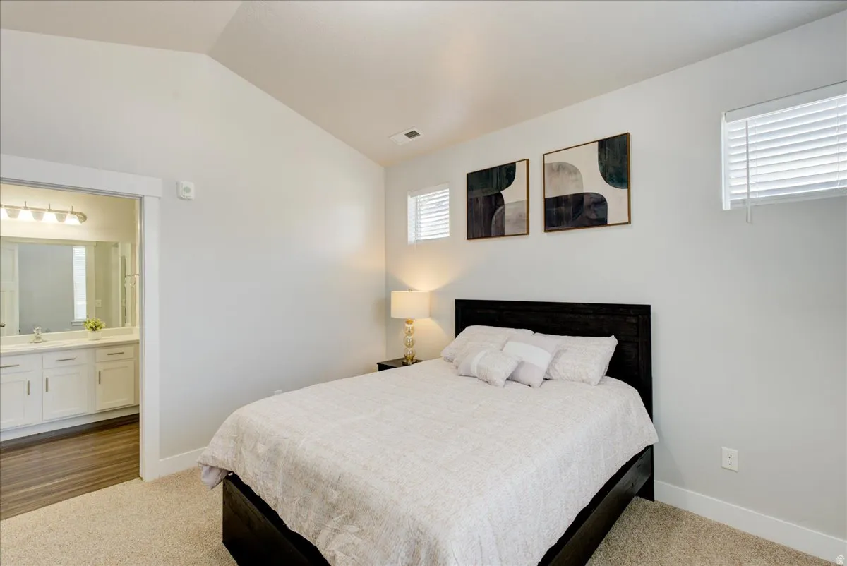 Bedroom with vaulted ceiling, dark colored carpet, and connected bathroom