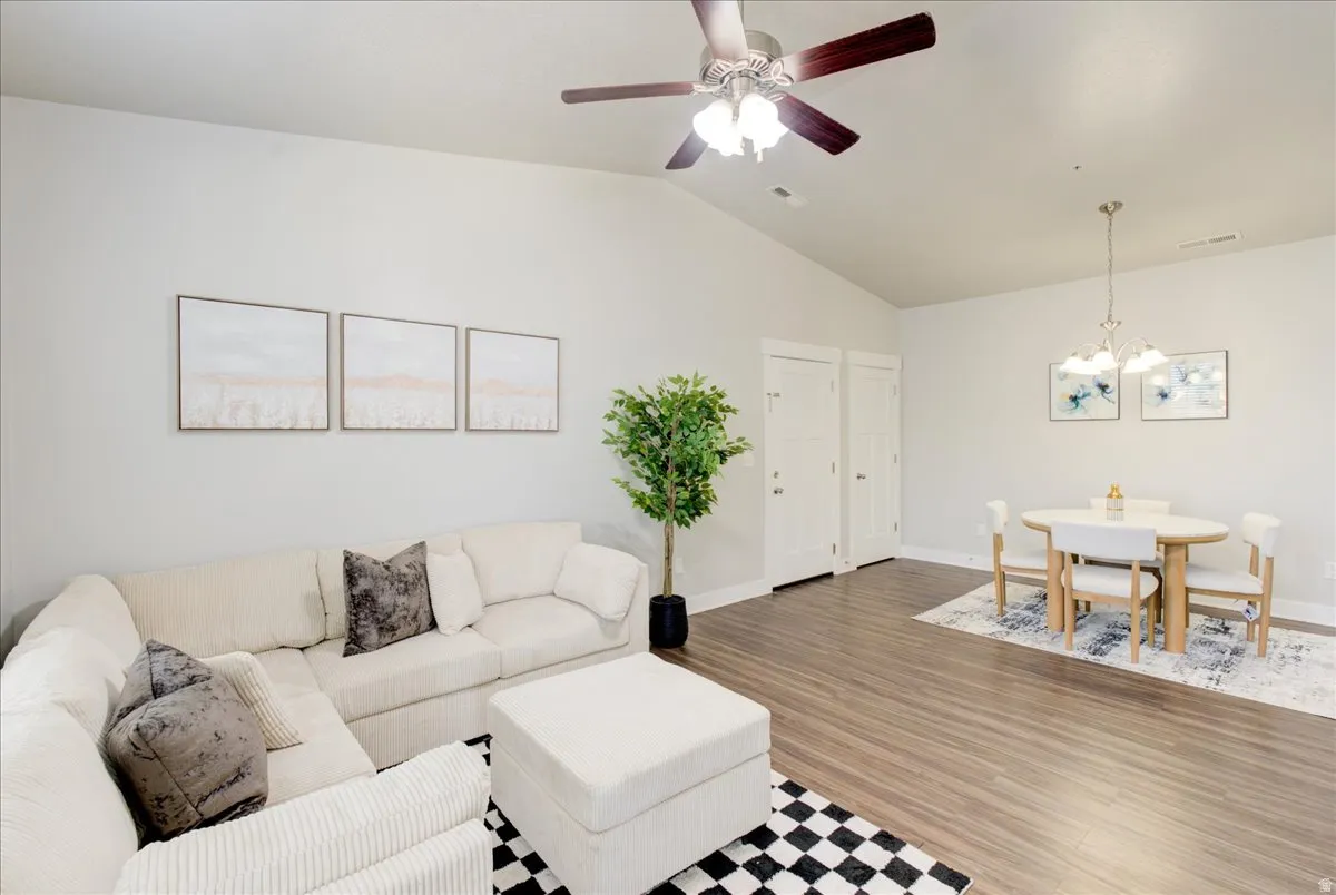 Living area featuring a ceiling fan, vaulted ceiling, suspended lighting, and wood finished floors