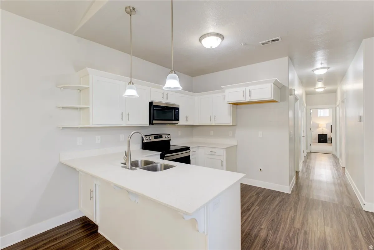 Kitchen with white cabinetry, stainless steel appliances, a peninsula, decorative light fixtures, and dark wood finished floors