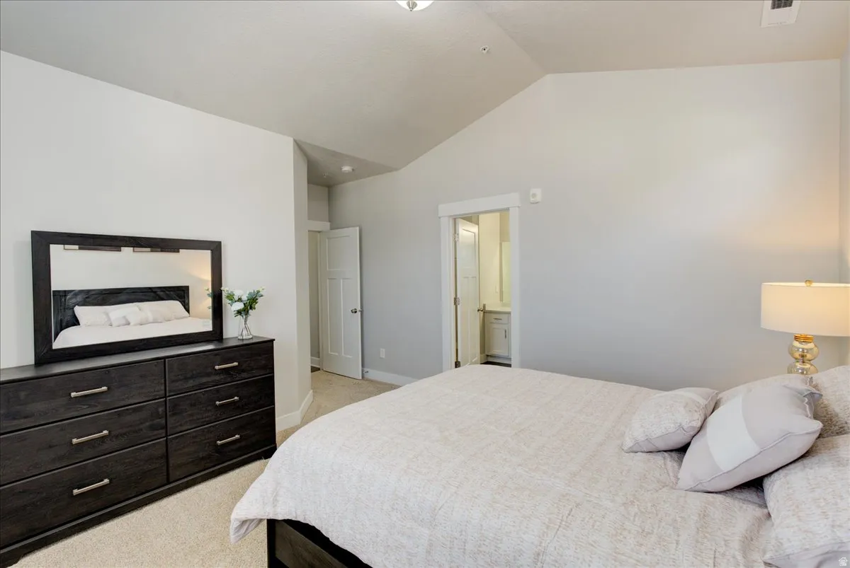 Bedroom featuring vaulted ceiling, light colored carpet, and ensuite bathroom