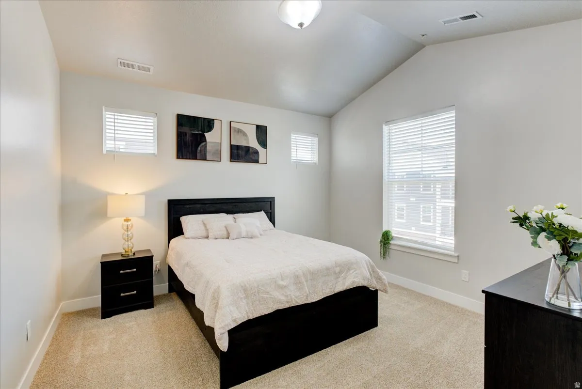 Bedroom with vaulted ceiling, light carpet, and multiple windows