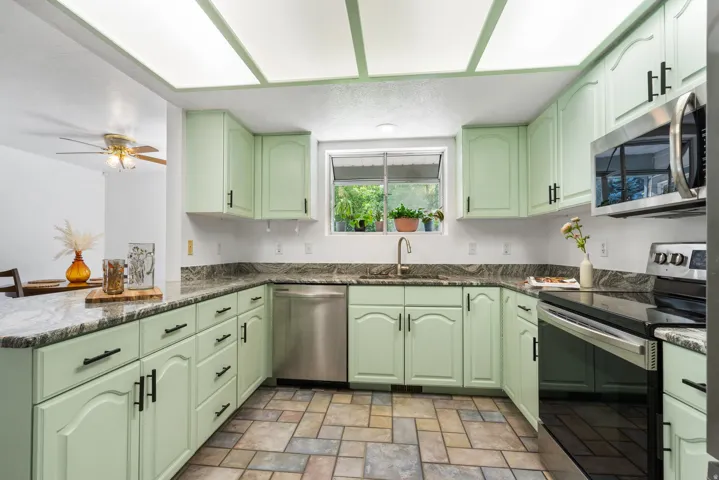 Kitchen featuring light green cabinetry, dark stone countertops, stainless steel appliances, a stainless steel sink, and tiled flooring