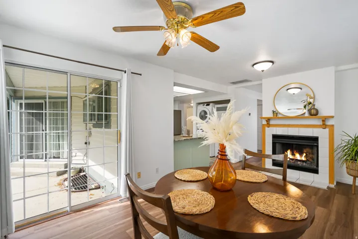 Wood-finish flooring throughout, sliding glass door, white tile fireplace surround, wood mantel, ceiling fan with integrated lighting