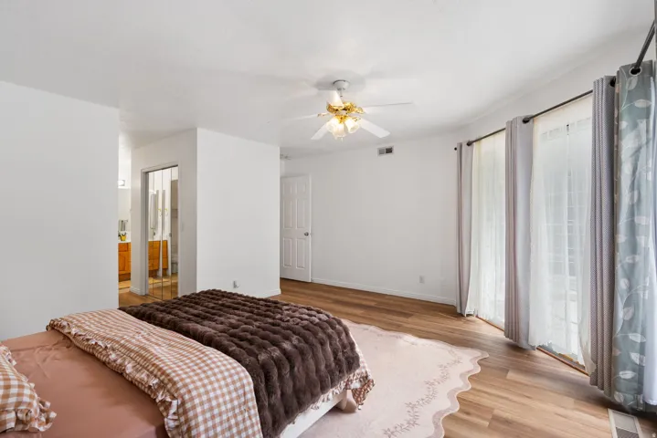 Wood-finish flooring, ceiling fan with illumination, white paneled door, and sliding glass doors