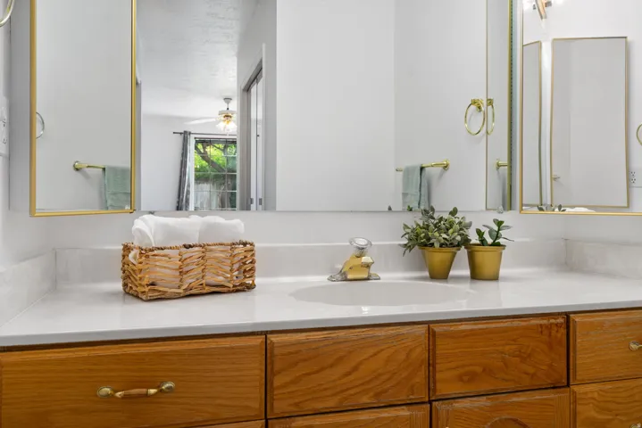 White countertop with an integrated sink, wood-finish cabinetry, and gold-framed mirrors
