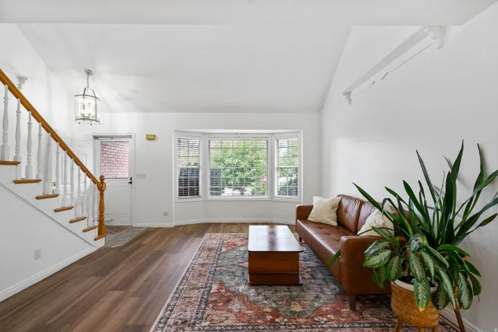 Vaulted ceilings, wood-finish flooring, white walls, bay windows, and a staircase with wood handrails
