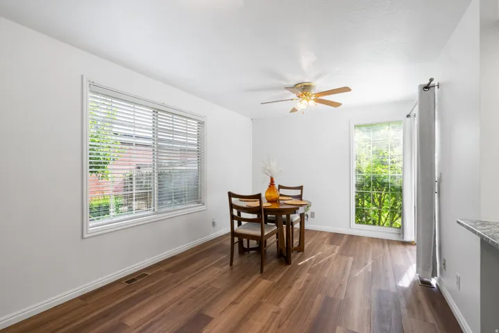 Wood-finish flooring, white walls, two windows with white trim, and a ceiling fan with integrated lighting
