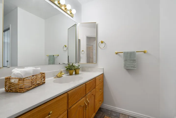 Bathroom vanity featuring a light-toned countertop with an integrated sink, wood-finish cabinetry, and a full-width mirror with overhead lighting