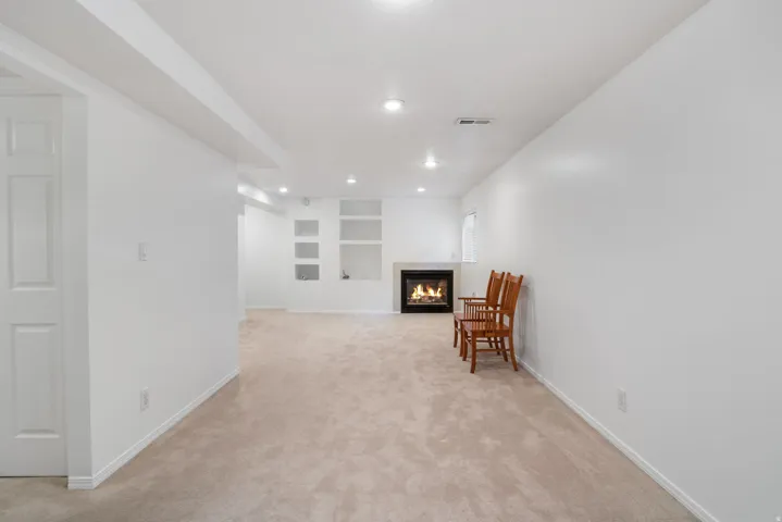 Living area with a tiled fireplace, built in features, light colored carpet, and recessed lighting