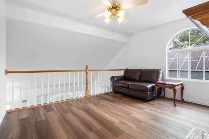 Sitting room with plenty of natural light, laminate wood-style flooring, ceiling fan, and vaulted ceiling