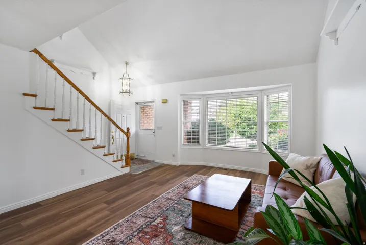 Bright, open foyer showcasing a wood-finish staircase with metal railings, hardwood flooring throughout, and abundant natural light from multi-pane glass doors and windows