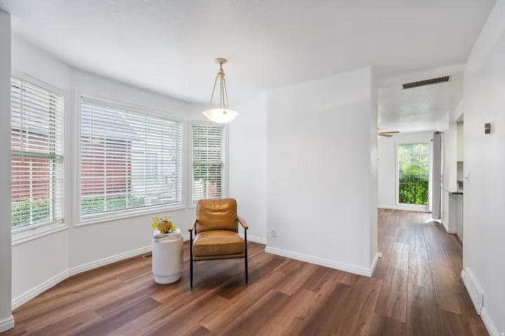 Bay window with white blinds, wood-finish flooring, white walls, and a ceiling-mounted light fixture