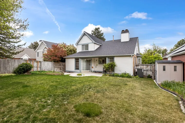 Rear view of house with a chimney, a patio, a shingled roof, a fenced backyard, and an outbuilding