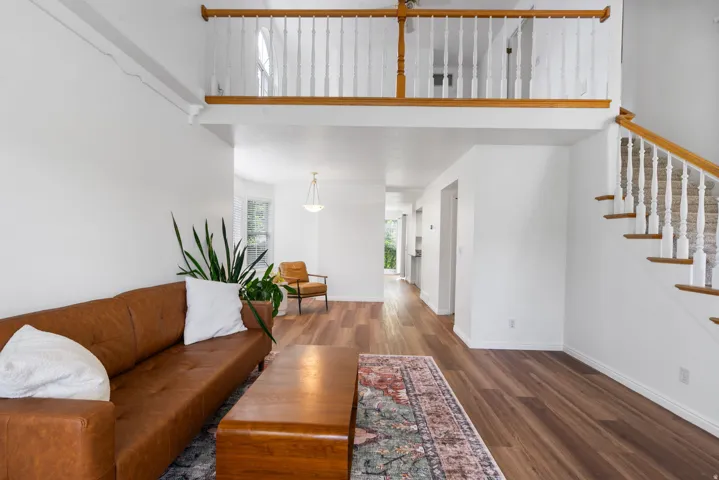 Wood-finish flooring throughout, bright white walls, open-concept living space, staircase with white balusters and wood handrail, and an upper-level railing